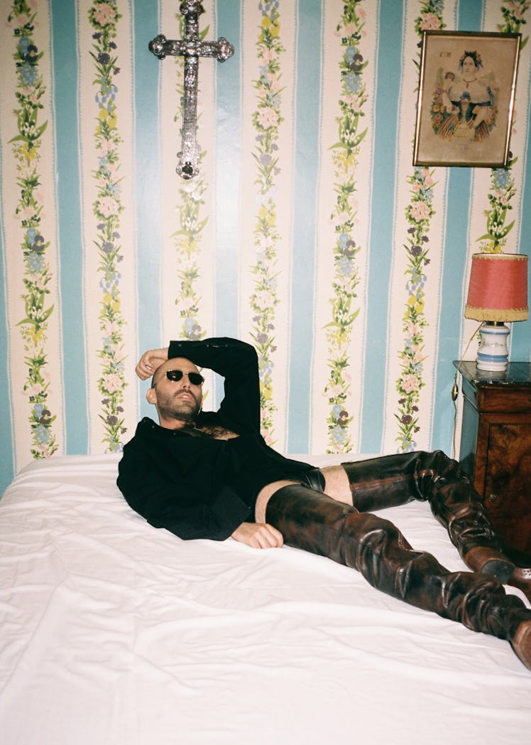 A model lying on a bed wearing a black sweatshirt, black sunglasses and black thigh-high leather boo...