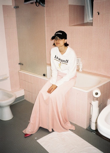 A model in a pink maxi skirt and white hoodie sitting on a bathtub in Vetements Summer Camp 