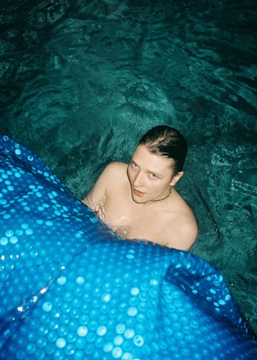 A model with wet slicked back hair looking at the camera from a pool at night 