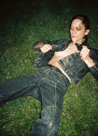 A woman lying on grass with a cigarette in her mouth