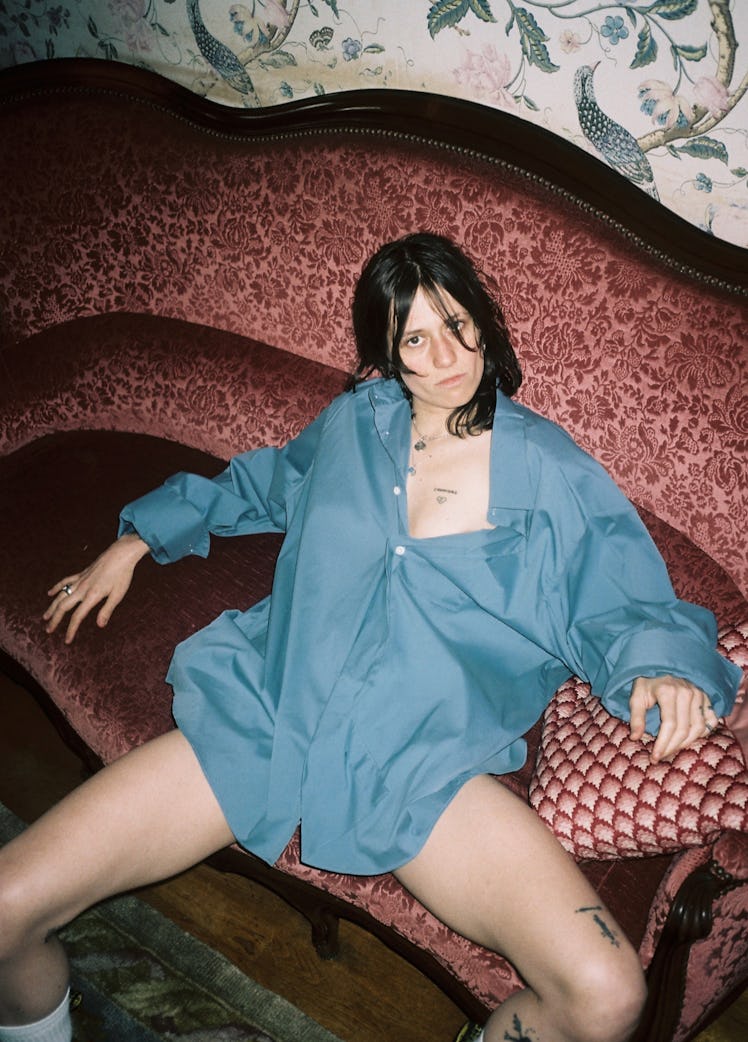 A model sitting on a couch in a blue oversized button-up