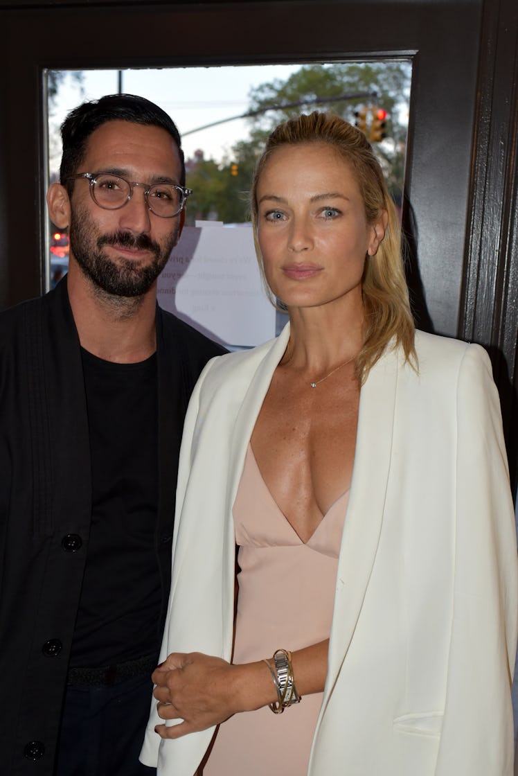 A blonde woman in a white blazer and pink dress posing with a man that is wearing a black blazer