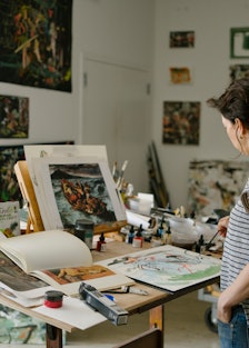 Cecily Brown standing and looking at her art in her New York studio