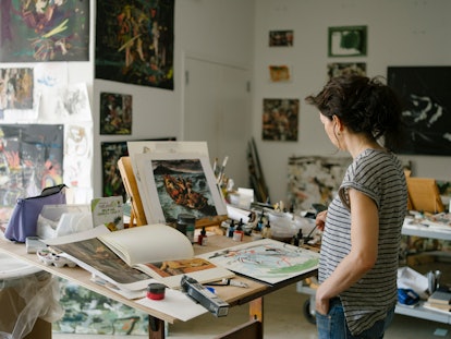 Cecily Brown standing and looking at her art in her New York studio