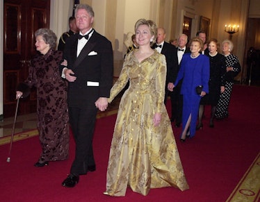 Hillary Clinton in a golden gown walking next to Bill Clinton in June 2002