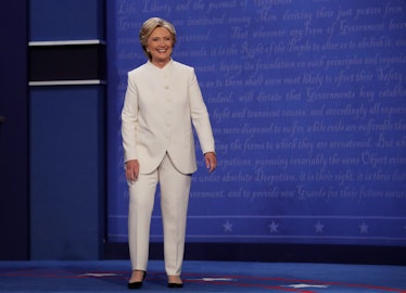 Hillary Clinton in a white suit and black pumps standing and smiling in October 2016