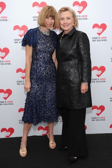 Hillary Clinton in a black shimmer coat and trousers posing next to Anna Wintour in a navy lace dres...