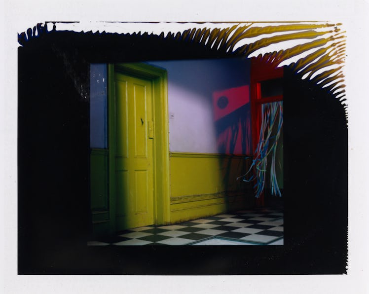 Miles Aldridge's polaroid featuring a room with a yellow door, white-yellow wall and a black-white c...