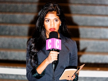 A newscaster with a pink microphone and a notepad reporting from the Jacob K. Javits Convention Cent...