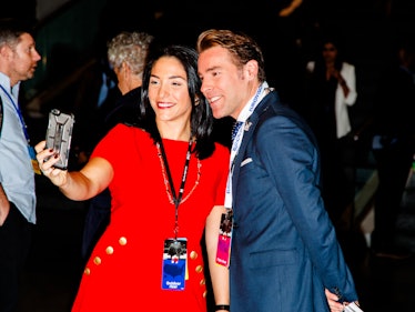 A woman in a red dress taking a selfie with a man in a navy blue blazer 