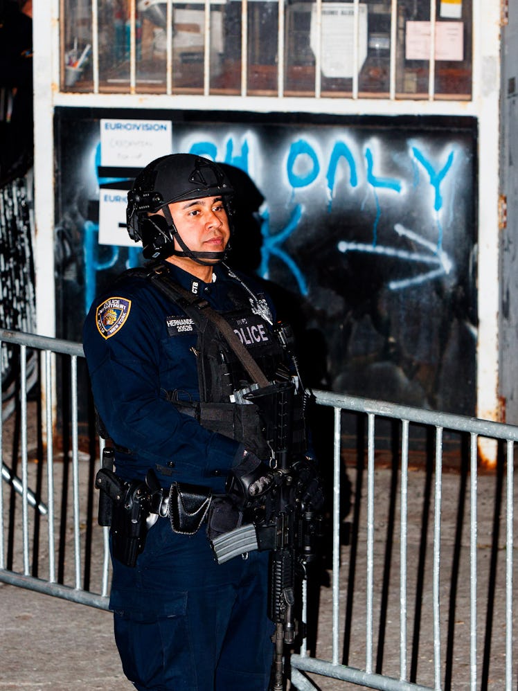 A police officer in uniform standing next to a fence at the A woman taking a video with her phone at...