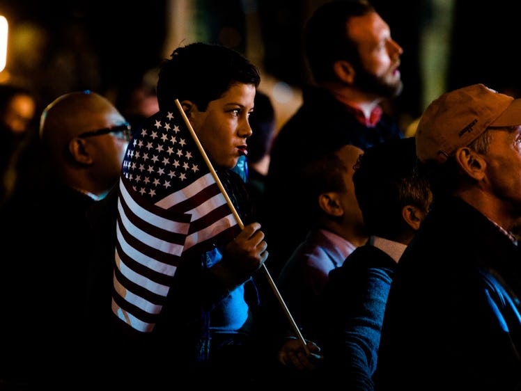 A closeup of a little boy in the crowd holding a U.S. flag and looking very focused at the election ...