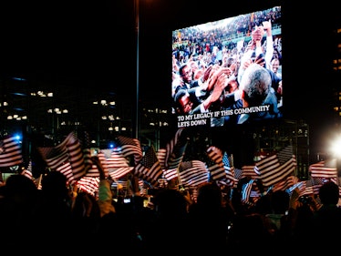 The crowd waving American flags as a large screen above them says "to my community if this legacy le...