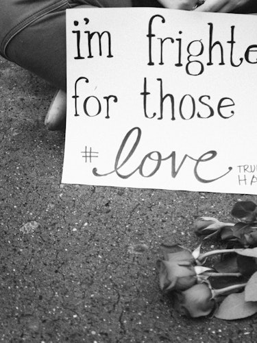 A white protest sign 'I'm frightened for those I #love' and a small bouquet of roses on the street