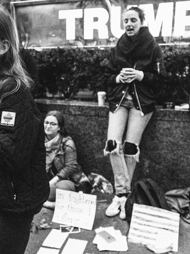 Five young protesters standing and sitting next to a short wall with protest signs
