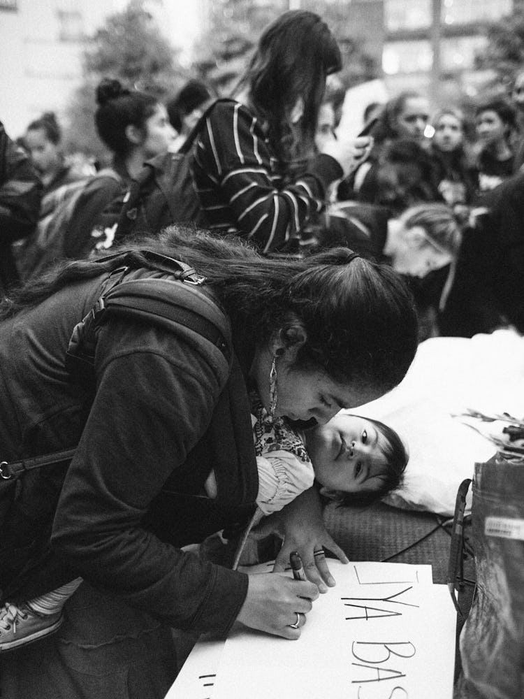 A woman leaning over a protest sign an writing on it with a child next to her