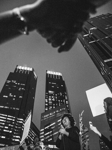 Two people holding hands and walking during a protest and tall buildings visible in the background