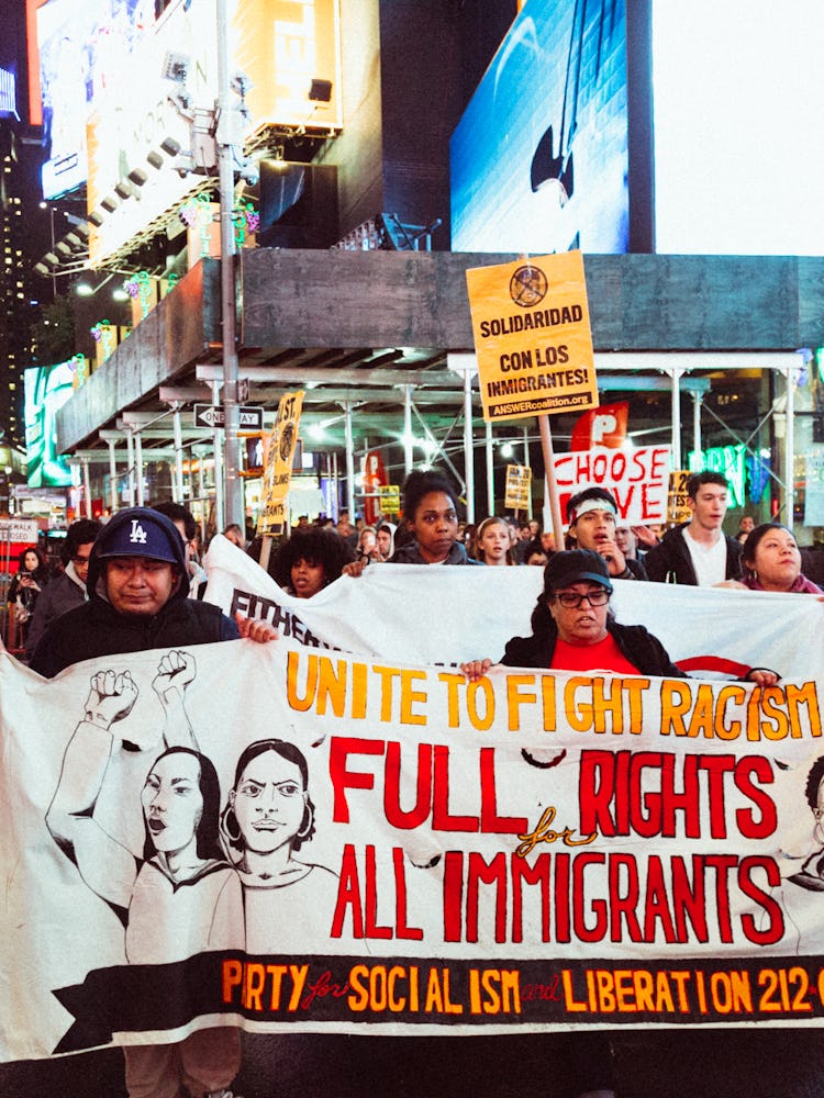 A large group of people marching while holding a white protest sign 'Unite to fight racism full righ...