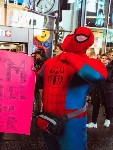 Two activists dressed as Spidermen holding a red sign with the text 'I'M STILL WITH HER'