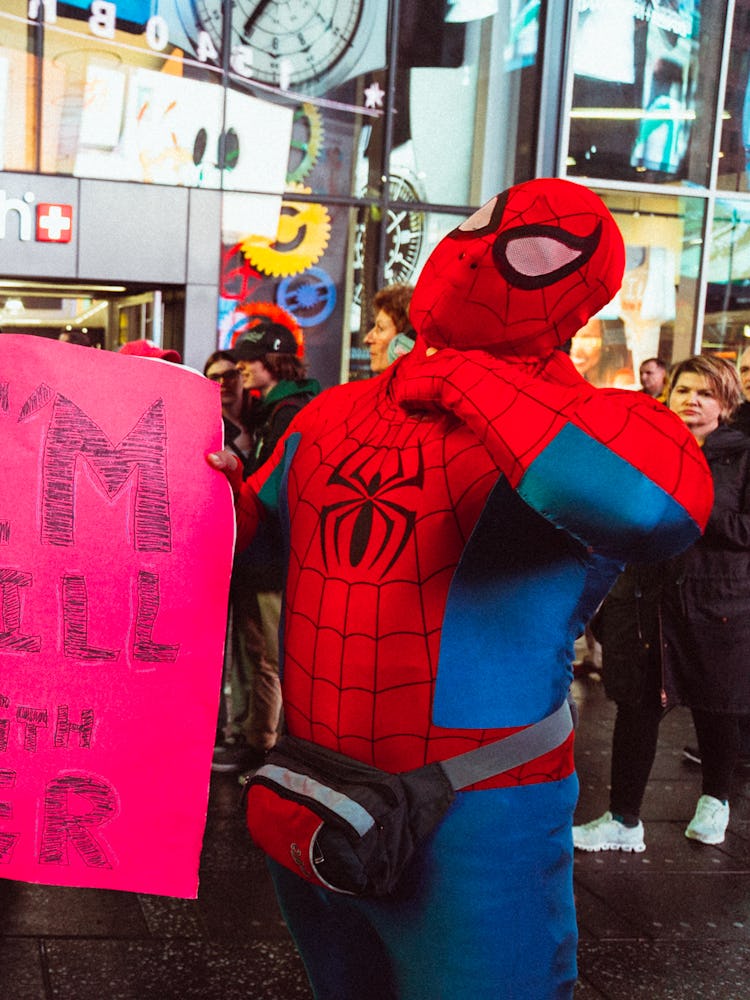Two activists dressed as Spidermen holding a red sign with the text 'I'M STILL WITH HER'