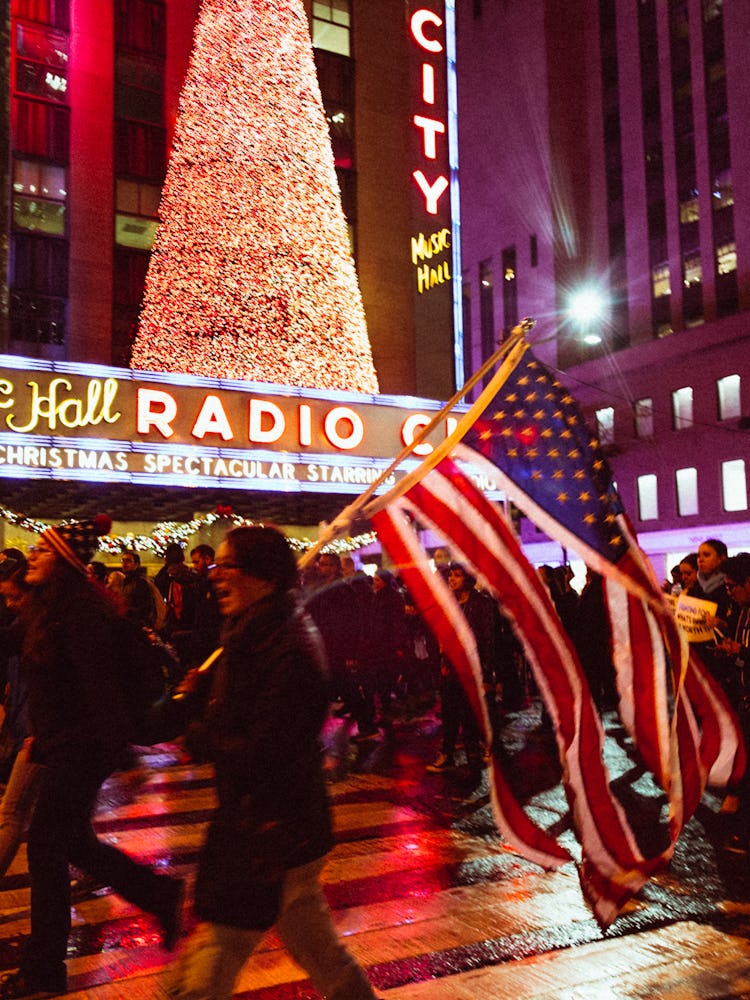 A group of activists marching during night time while carrying a torn American flag