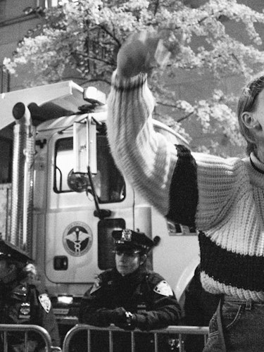 A woman in a sweater yelling and waving with her arms and police officers standing in the background
