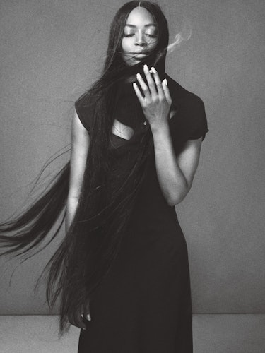 Naomi Campbell in a black dress standing while smoking a cigarette
