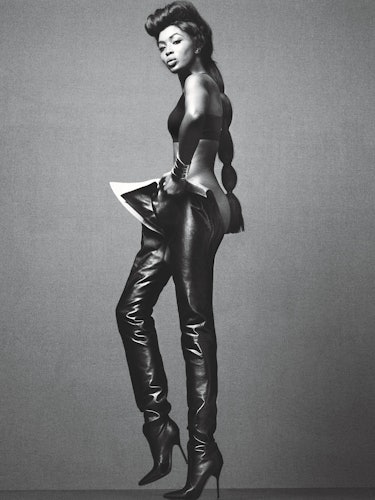 Naomi Campbell standing and posing in black leather trouser boots and a black bralette