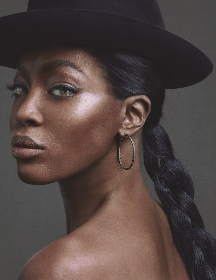 A portrait of Naomi Campbell with braided hair, a black hat and hoop earrings