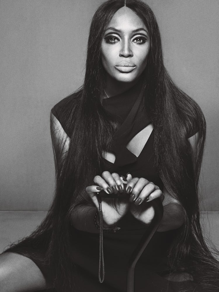 Naomi Campbell sitting and posing in a black dress