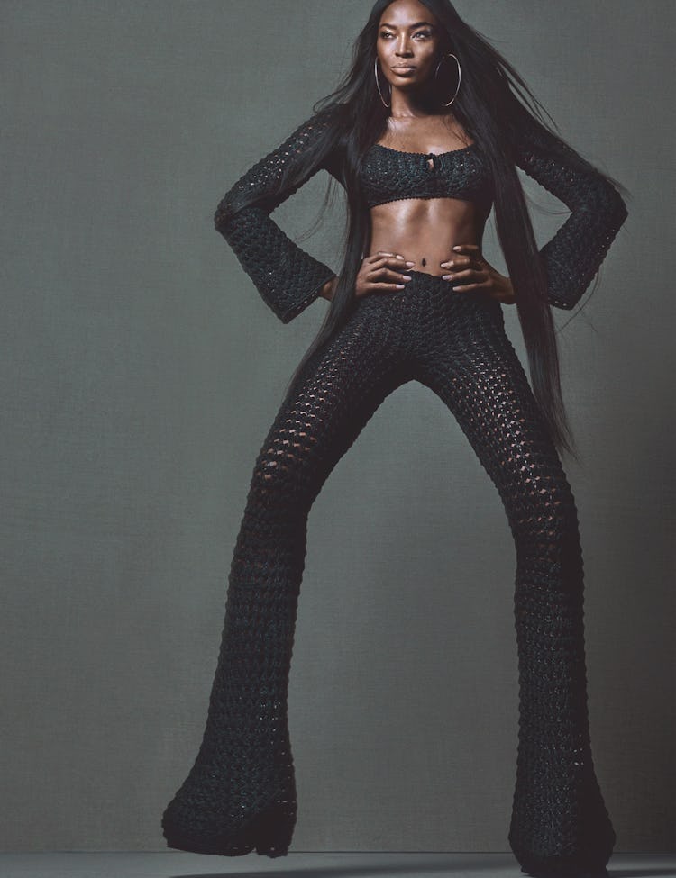 Naomi Campbell posing in a black knit top and trousers