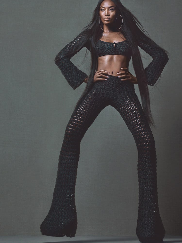 Naomi Campbell posing in a black knit top and trousers