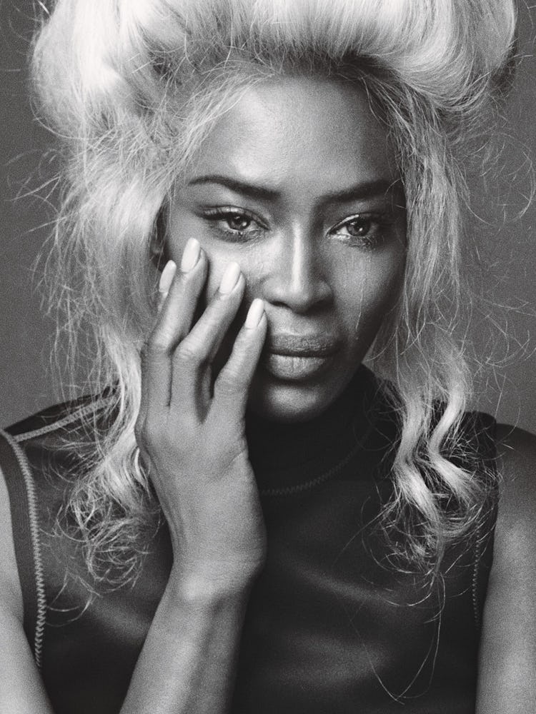 A portrait of Naomi Campbell in a black dress and a blonde wig