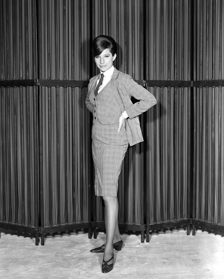 Barbra Streisand in a checked blazer, skirt and waistcoat and black shoes standing and posing