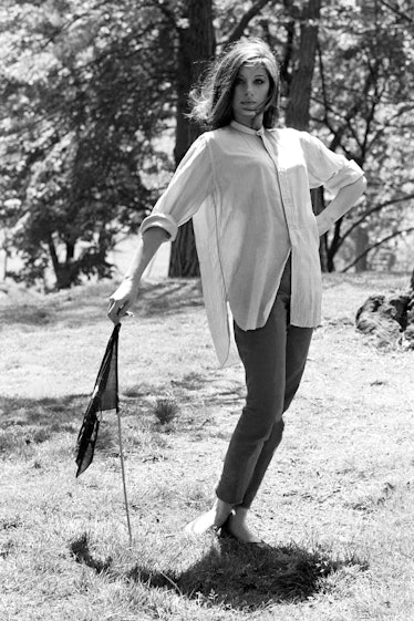 Barbra Streisand posing in a white shirt and black trousers outside while leaning onto a small flag