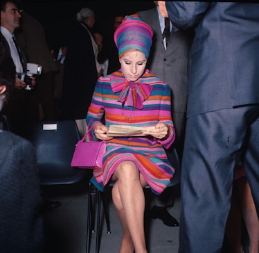 Barbra Streisand in a pink-blue-orange striped dress with bow, matching head piece and a pink bag in...
