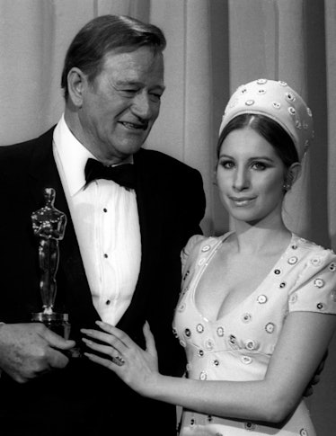 John Wayne in a black blazer, white shirt and black bowtie and Barbra Streisand in a white dress wit...