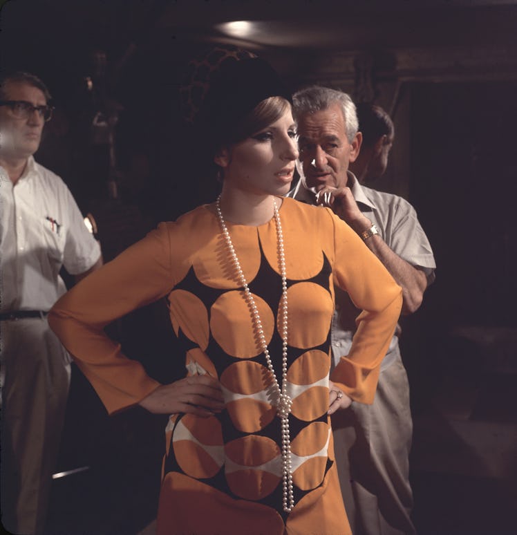 Streisand wearing an orange dress and a long pearl necklace on the set of “Funny Girl” 