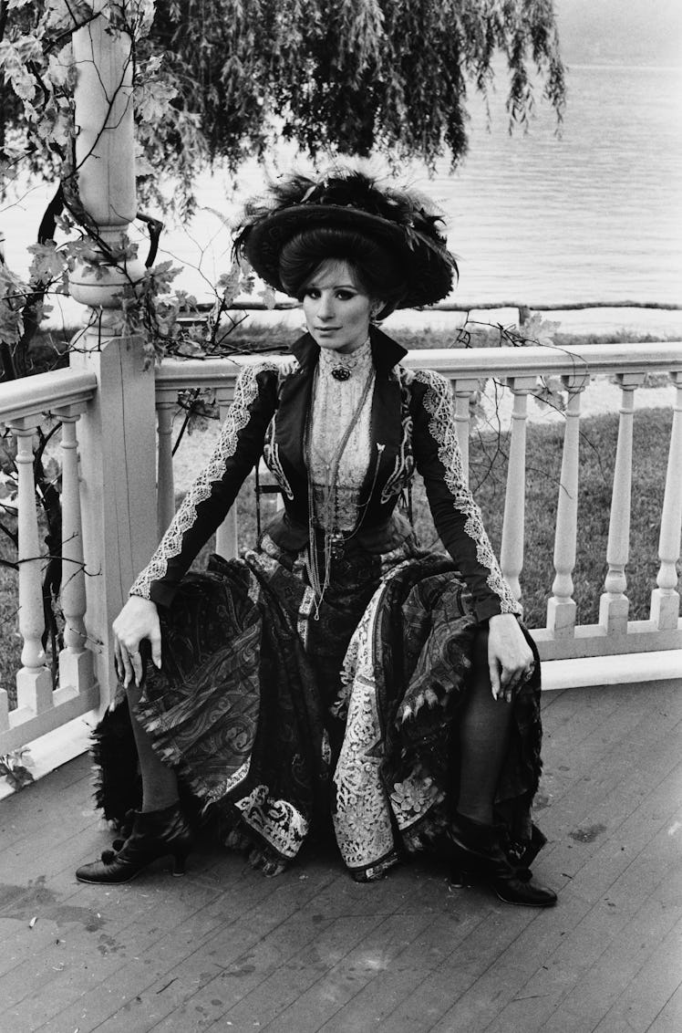 Streisand dressed in an embroidered gown with a hat covered in feathers 
