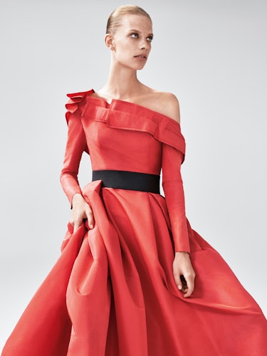 A model wearing a red asymmetric dress with a black belt by Carolina Herrera
