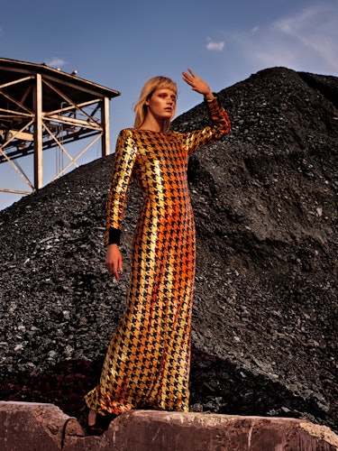 A model in a gold-black sequin gown posing on a construction site
