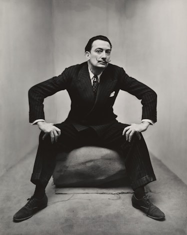 Salvador Dali sitting while wearing a formal suit