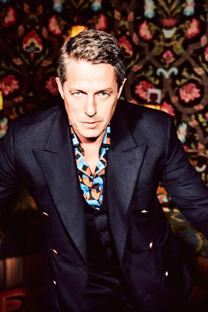 Hugh Grant posing in a black blazer and blue-orange-black shirt