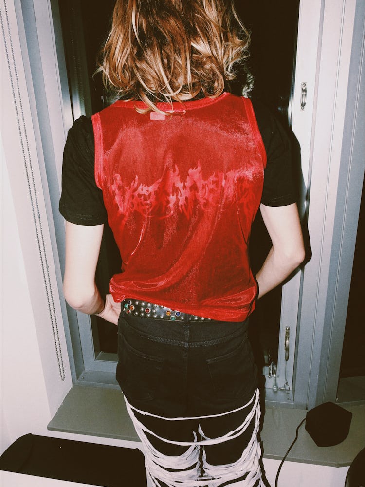 A  person with their back turned wearing a black shirt, red tank over it, black jeans and a studded ...