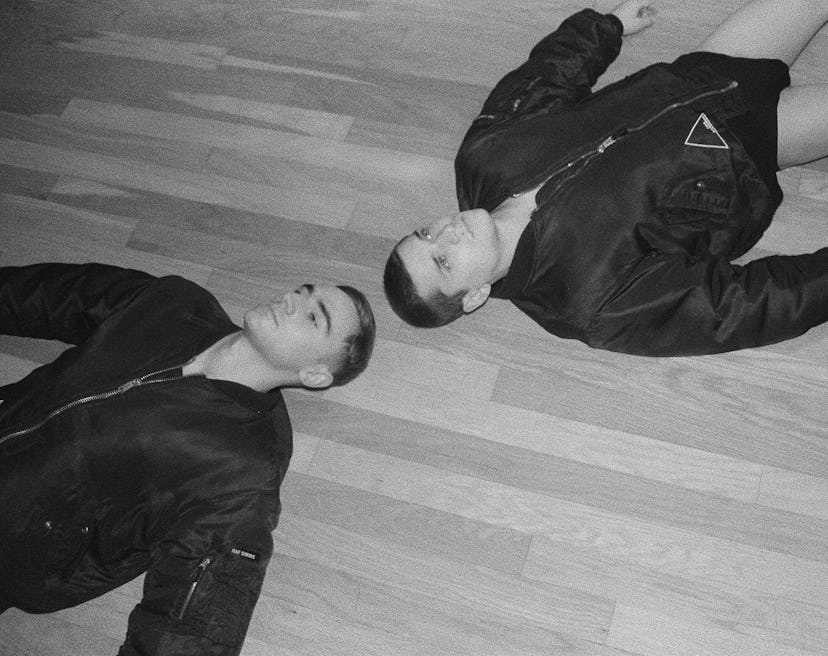 Two men lying on the floor in matching black puffer coats