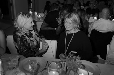 Susan Margrino & Martha Stewart in black dresses sitting at a dinner table and having a conversation