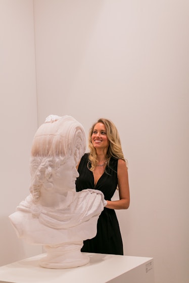 A woman in a black dress standing next to a bust displayed at the Art Basel Miami Beach 2016