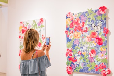 A woman taking a photo of paintings at the Art Basel Miami Beach 2016