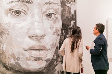 Two people looking at a large painting of a woman's face at the Art Basel Miami Beach 2016