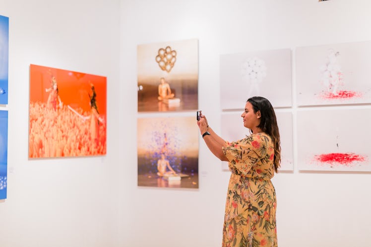 A woman taking photos of paintings displayed at the Art Basel Miami Beach 2016